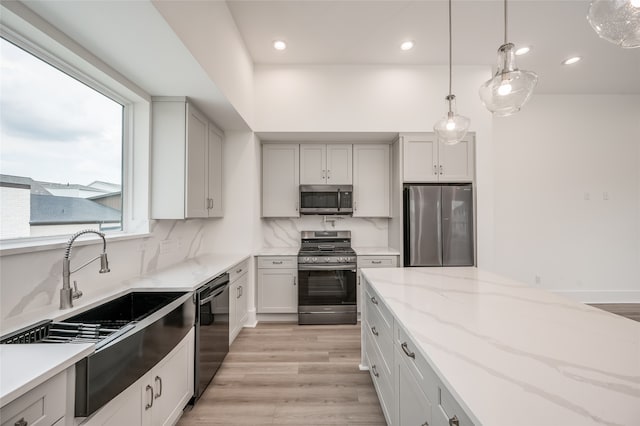 kitchen with pendant lighting, light hardwood / wood-style flooring, white cabinetry, stainless steel appliances, and light stone countertops