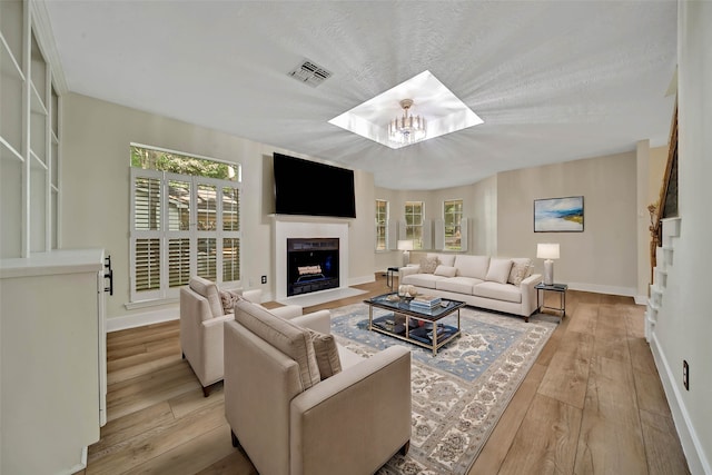 living room featuring light wood-type flooring, a chandelier, and a textured ceiling