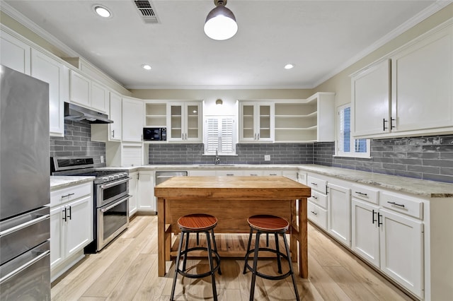 kitchen with light wood-type flooring, ornamental molding, white cabinetry, stainless steel appliances, and light stone countertops