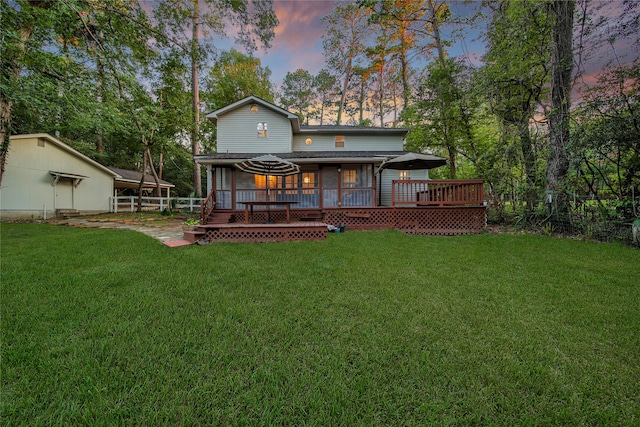 back house at dusk featuring a wooden deck and a yard