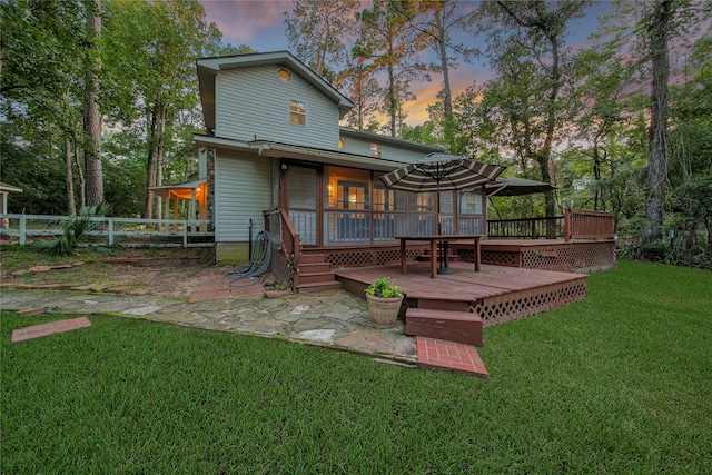 back house at dusk featuring a yard, a sunroom, and a wooden deck