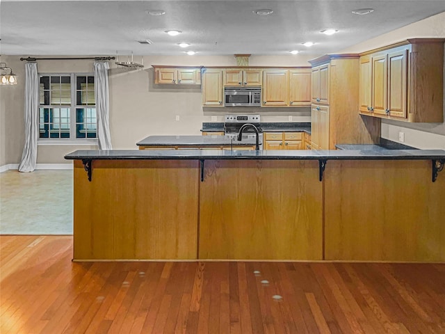 kitchen featuring sink, a breakfast bar area, kitchen peninsula, stainless steel appliances, and hardwood / wood-style floors