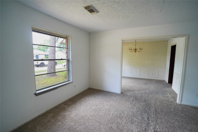 carpeted spare room featuring a notable chandelier and a textured ceiling