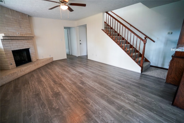 unfurnished living room featuring a brick fireplace, a textured ceiling, ceiling fan, and dark hardwood / wood-style flooring