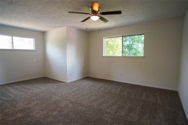 unfurnished room featuring a textured ceiling, dark carpet, and plenty of natural light