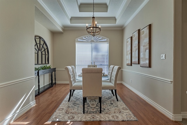 dining space featuring wood-type flooring, a tray ceiling, an inviting chandelier, and ornamental molding