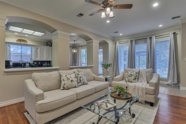 living room with wood-type flooring, ceiling fan with notable chandelier, decorative columns, and ornamental molding