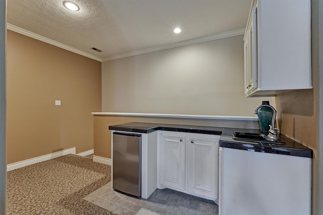 kitchen with white cabinets, crown molding, stainless steel fridge, light tile patterned floors, and a textured ceiling