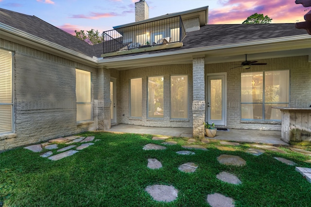 back house at dusk with a yard, ceiling fan, and a balcony