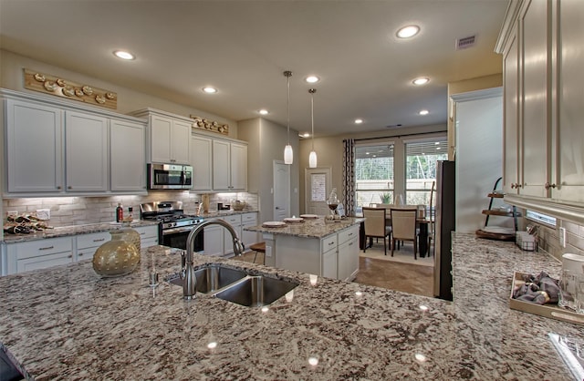 kitchen with pendant lighting, sink, light stone countertops, appliances with stainless steel finishes, and a kitchen island