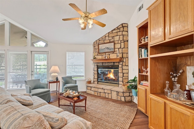 living room with dark hardwood / wood-style floors, built in shelves, lofted ceiling, a stone fireplace, and ceiling fan