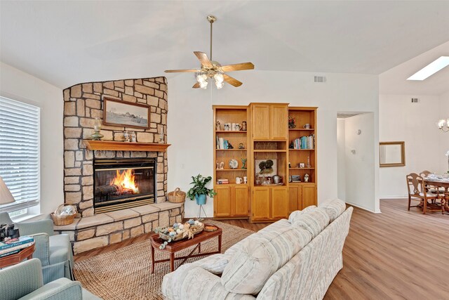 living room featuring vaulted ceiling with skylight, light hardwood / wood-style floors, ceiling fan, and a stone fireplace