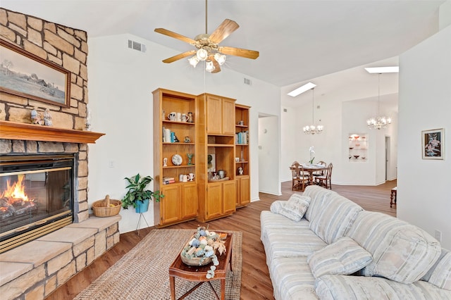 living room with ceiling fan with notable chandelier, lofted ceiling, a fireplace, and hardwood / wood-style floors