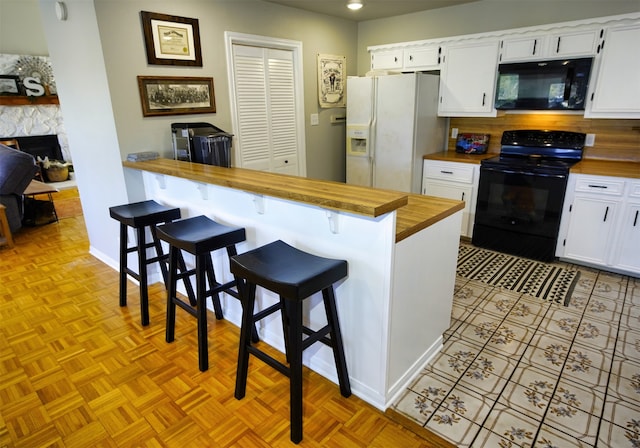 kitchen with a breakfast bar area, black appliances, wooden counters, and white cabinetry