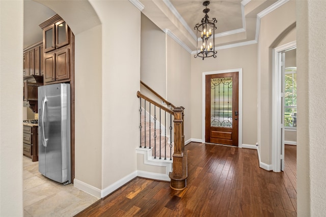 entrance foyer with light wood-type flooring, ornamental molding, a tray ceiling, and a notable chandelier