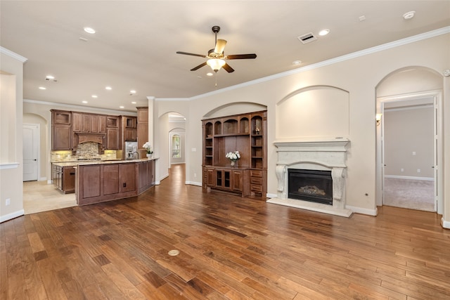 living room featuring light wood-type flooring, a premium fireplace, ceiling fan, and crown molding