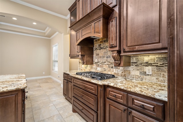 kitchen featuring light stone counters, tasteful backsplash, stainless steel gas cooktop, a tray ceiling, and ornamental molding