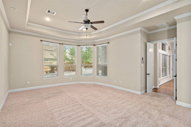 empty room featuring ceiling fan, light colored carpet, a tray ceiling, and ornamental molding