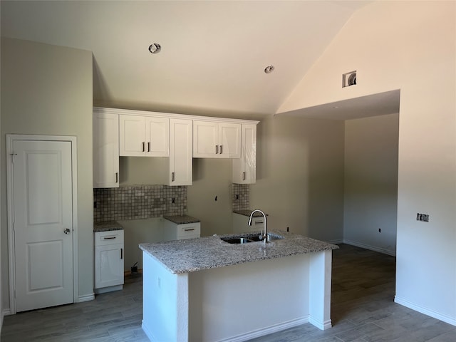 kitchen with white cabinetry, light stone countertops, sink, and a center island with sink