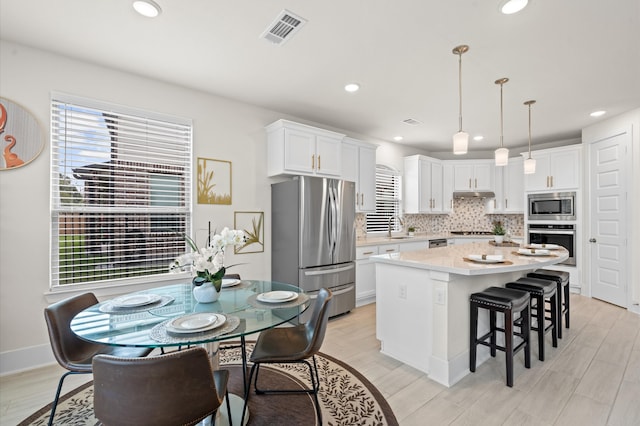 kitchen with white cabinetry, hanging light fixtures, a kitchen island, decorative backsplash, and stainless steel appliances