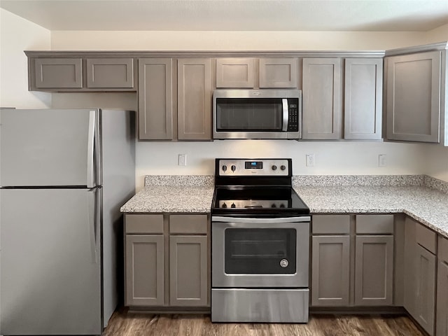 kitchen featuring light stone countertops, gray cabinets, appliances with stainless steel finishes, and dark hardwood / wood-style flooring