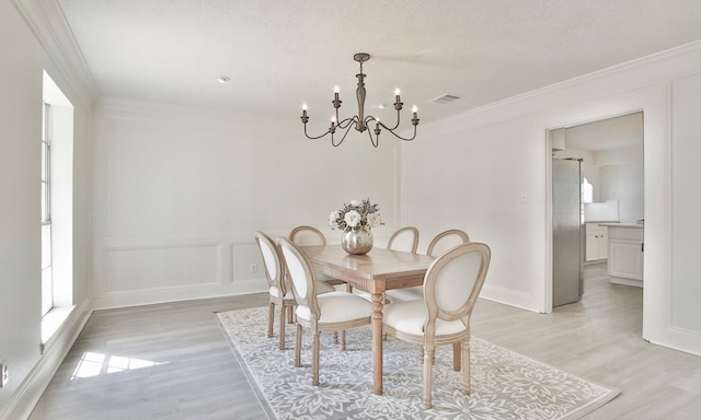 dining room with light wood-type flooring, crown molding, and a notable chandelier