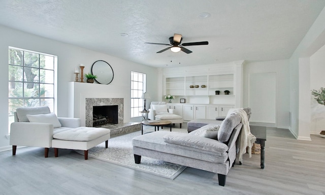 living room with light hardwood / wood-style flooring, a premium fireplace, ceiling fan, and a textured ceiling