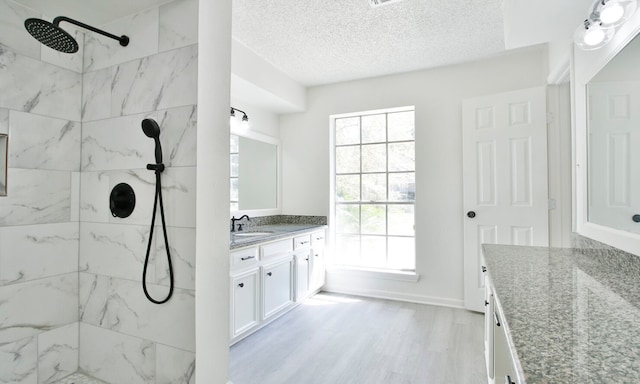 bathroom with a tile shower, a textured ceiling, hardwood / wood-style flooring, and vanity