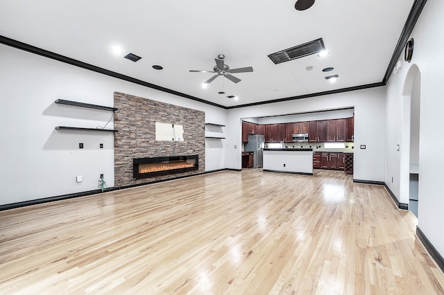 unfurnished living room with ceiling fan, a stone fireplace, crown molding, and light hardwood / wood-style floors