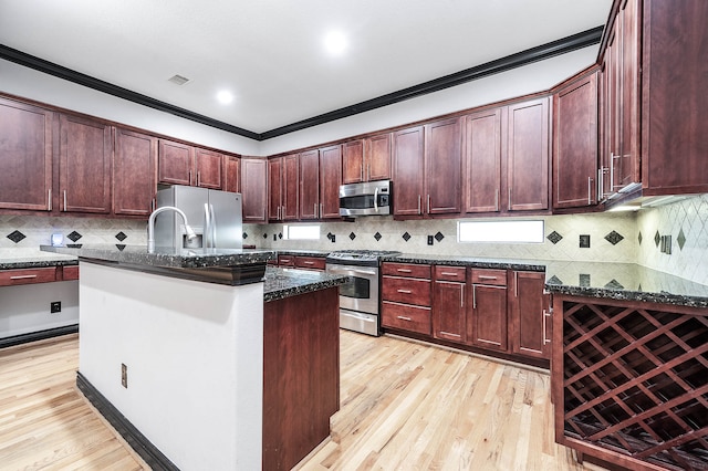 kitchen with dark stone counters, stainless steel appliances, a kitchen island with sink, and crown molding