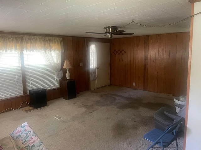 unfurnished living room with wood walls, ceiling fan, and carpet floors