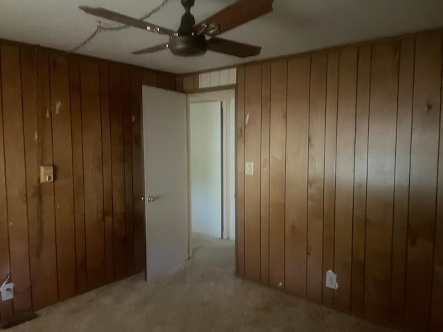 spare room with ceiling fan, wood walls, and light carpet