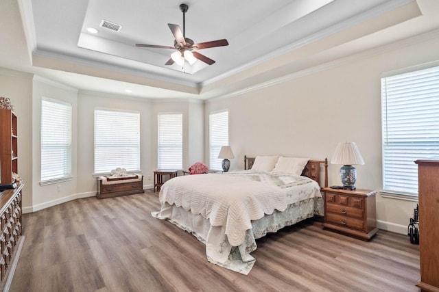bedroom featuring multiple windows, a tray ceiling, visible vents, and light wood-style flooring