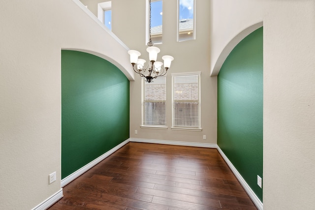 unfurnished room featuring a high ceiling, an inviting chandelier, and dark wood-type flooring