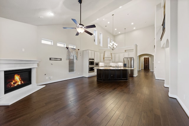 unfurnished living room featuring ceiling fan with notable chandelier, dark hardwood / wood-style flooring, sink, and high vaulted ceiling