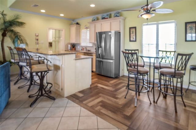 kitchen with ceiling fan, stone counters, stainless steel refrigerator with ice dispenser, light parquet floors, and a breakfast bar area