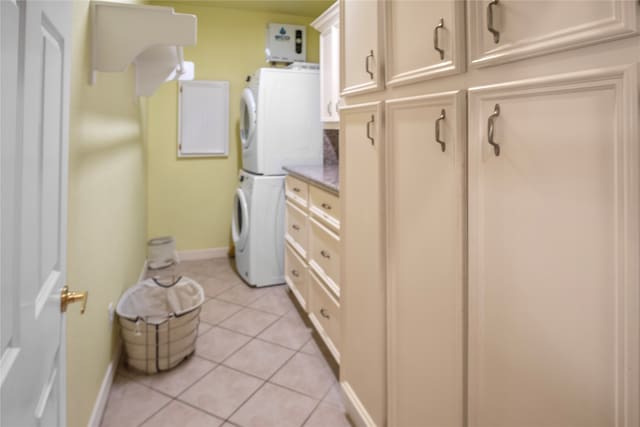 clothes washing area featuring cabinets, stacked washer / dryer, and light tile patterned floors