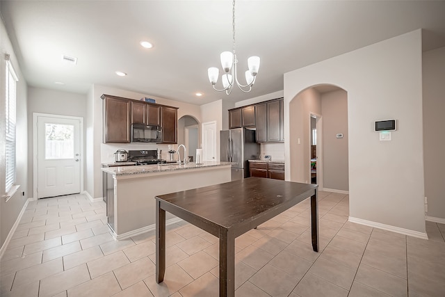 kitchen with decorative light fixtures, a center island with sink, a chandelier, black appliances, and light stone countertops