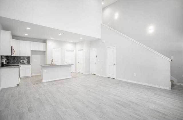 unfurnished living room with light wood-type flooring, high vaulted ceiling, ornamental molding, and sink