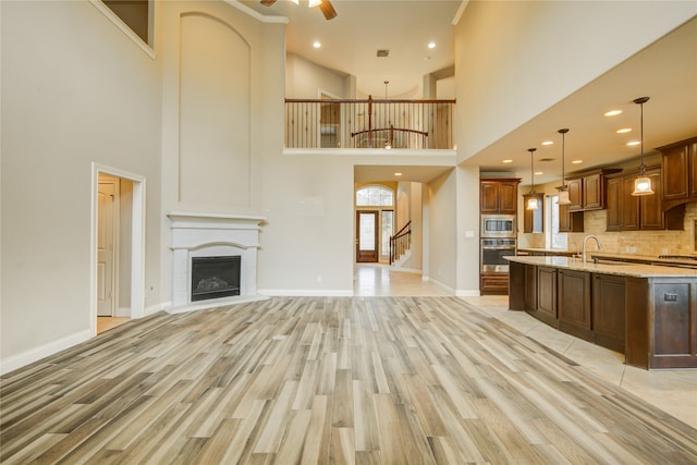 kitchen with appliances with stainless steel finishes, decorative light fixtures, light stone countertops, a high ceiling, and ceiling fan