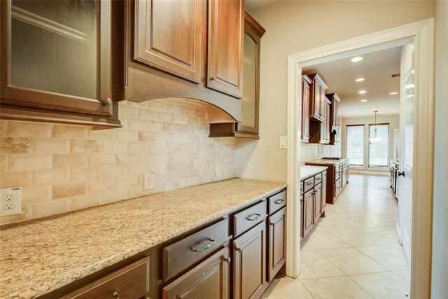 kitchen featuring hanging light fixtures, backsplash, light tile patterned floors, and light stone counters