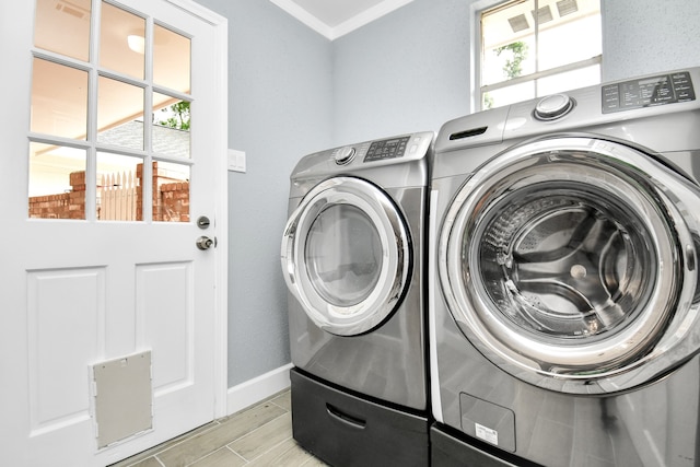 clothes washing area with crown molding, washing machine and dryer, and light hardwood / wood-style flooring