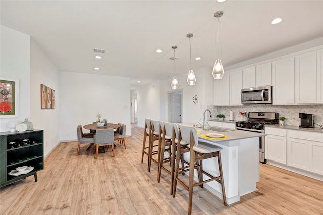 kitchen featuring sink, white cabinets, hanging light fixtures, stainless steel appliances, and a center island with sink