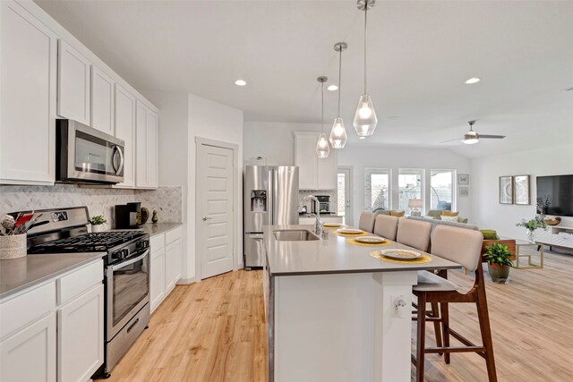 kitchen with ceiling fan, white cabinets, a center island with sink, stainless steel appliances, and light wood-type flooring