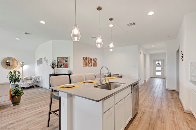 kitchen featuring sink, an island with sink, white cabinetry, light hardwood / wood-style flooring, and decorative light fixtures