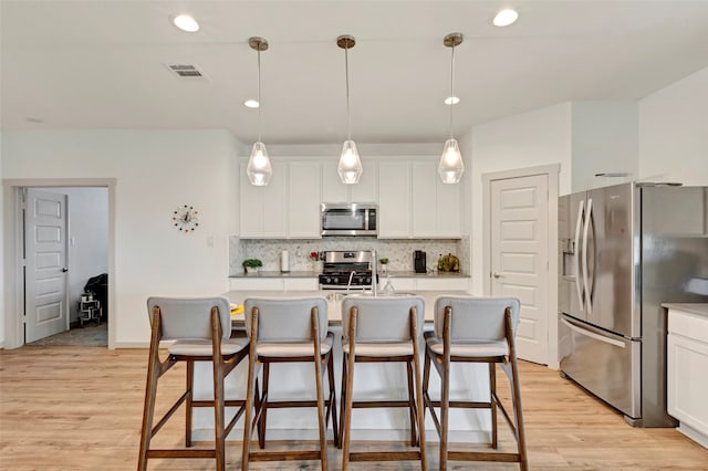 kitchen with appliances with stainless steel finishes, hanging light fixtures, light wood-type flooring, and an island with sink