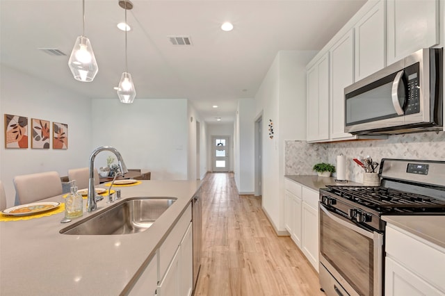 kitchen with pendant lighting, sink, white cabinetry, light hardwood / wood-style flooring, and stainless steel appliances