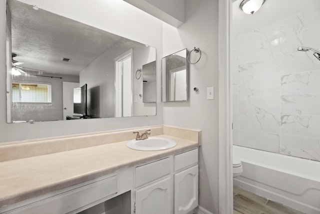 full bathroom with hardwood / wood-style flooring, vanity, ceiling fan, tiled shower / bath, and toilet