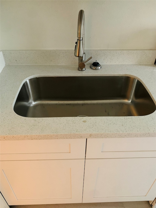 details with white cabinetry, light stone counters, and sink