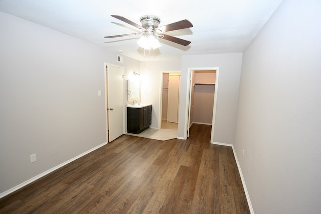 unfurnished bedroom featuring ceiling fan, hardwood / wood-style floors, a walk in closet, a closet, and ensuite bathroom